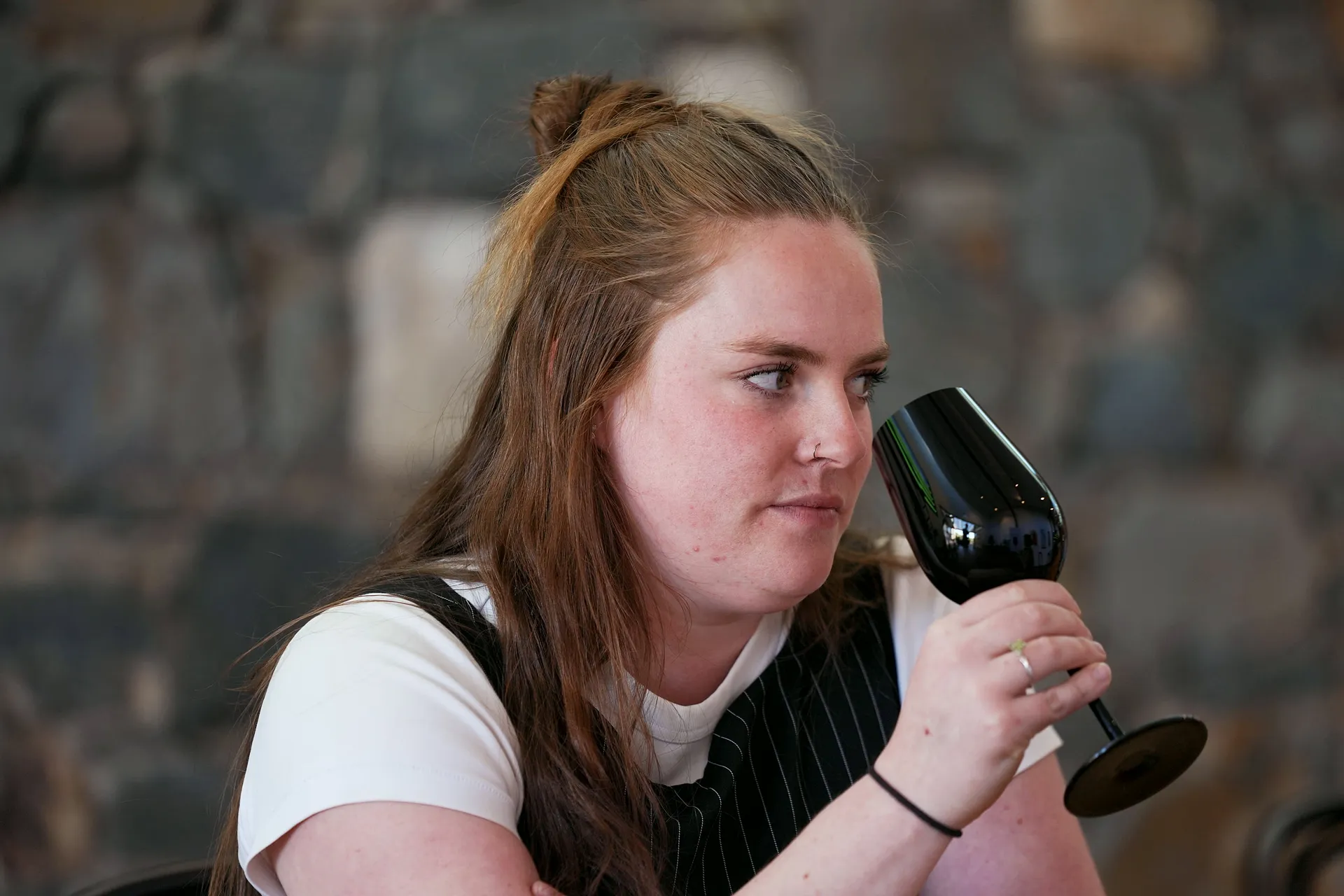 A Blackout player noses a black glass, eyes to one side, the stone wall of The Barossa Cellar soft behind.